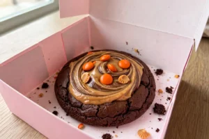 Crumbl Chocolate Peanut Butter Brownie cookie with Reese's Pieces candies in a pink Crumbl box