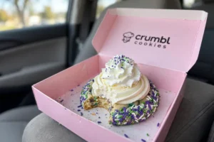 Crumbl Halloween Confetti Milkshake Cookie with a bite taken, in a pink Crumbl box on a car seat