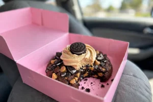 Crumbl Chocolate Peanut Butter Cookie ft. OREO with a bite taken, in a pink Crumbl box on a car seat