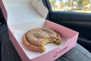 Crumbl Snickerdoodle Cookie with a bite taken, in a pink Crumbl box on a car seat